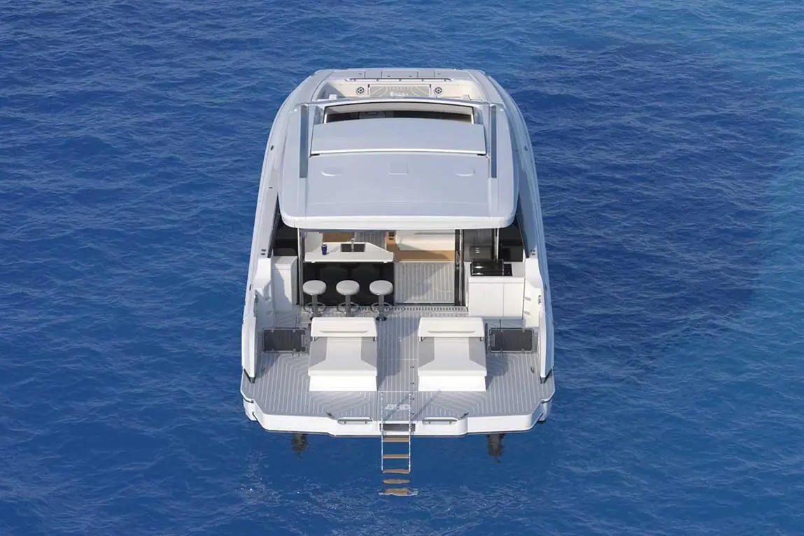 Aerial view of a modern yacht with sun loungers, a bar area, and a ladder, moored in deep blue sea.